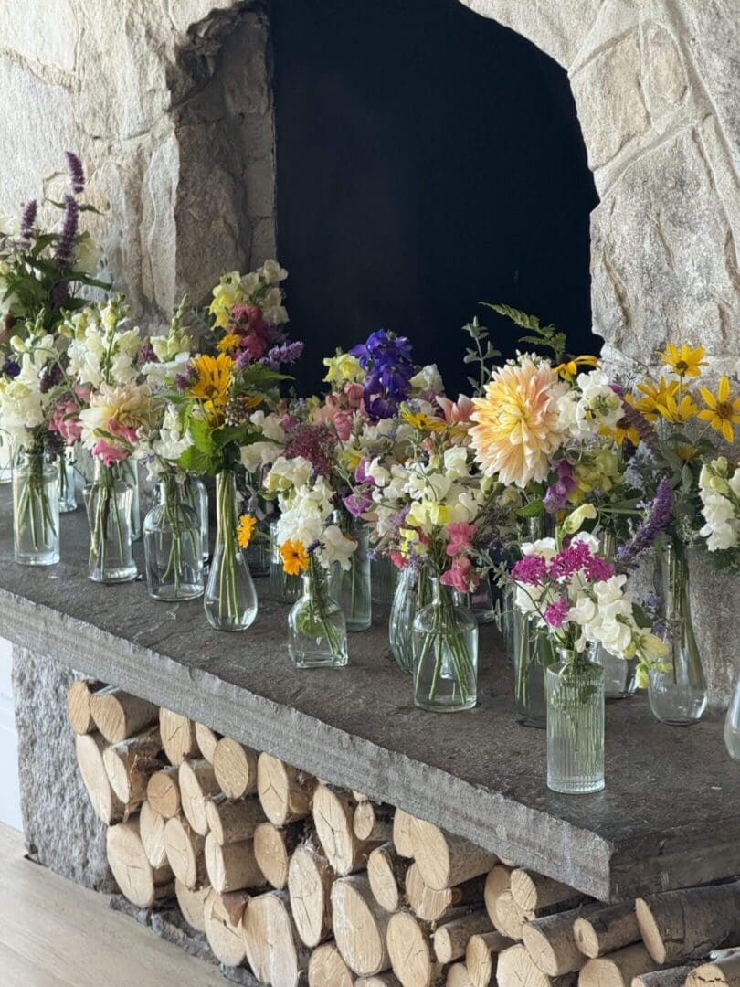 Flowers in vases on stone fireplace mantel.
