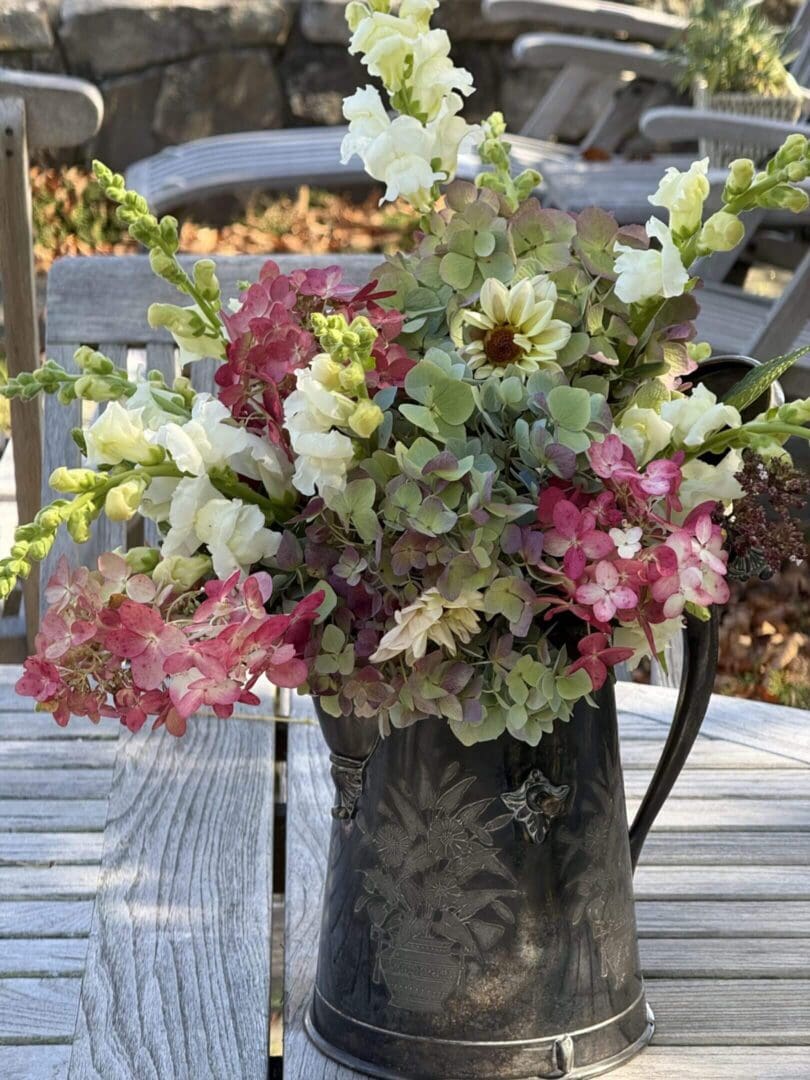 Flowers in decorative metal pitcher on table.