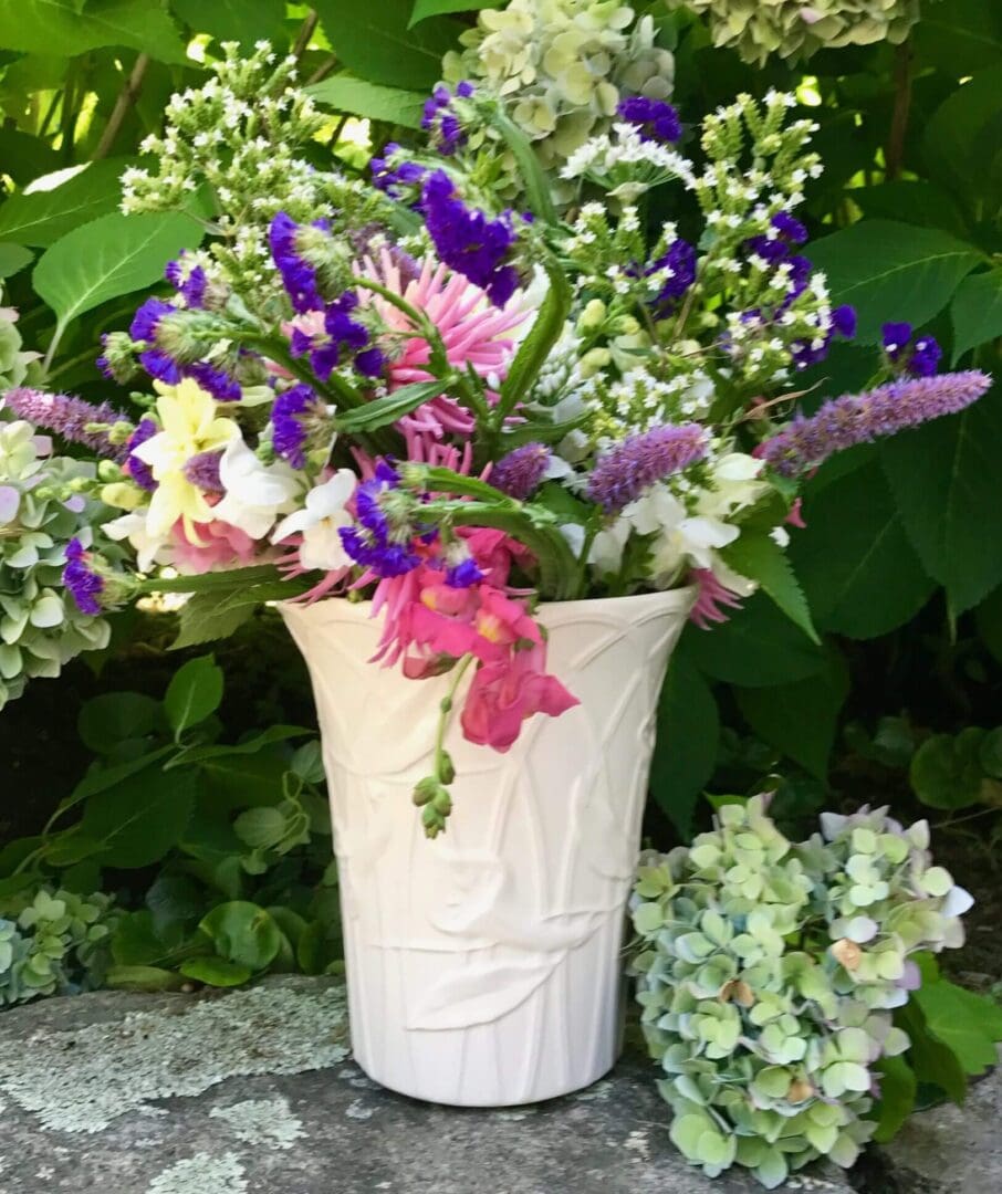 Colorful flowers in white vase, outdoor setting.
